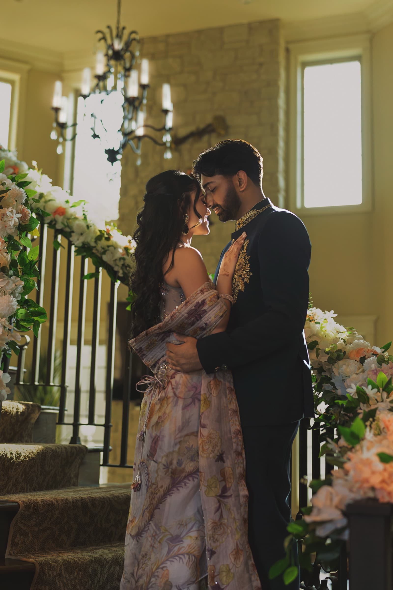 Aniketa and Dhruv embrace on a floral-lined staircase at their engagement celebration