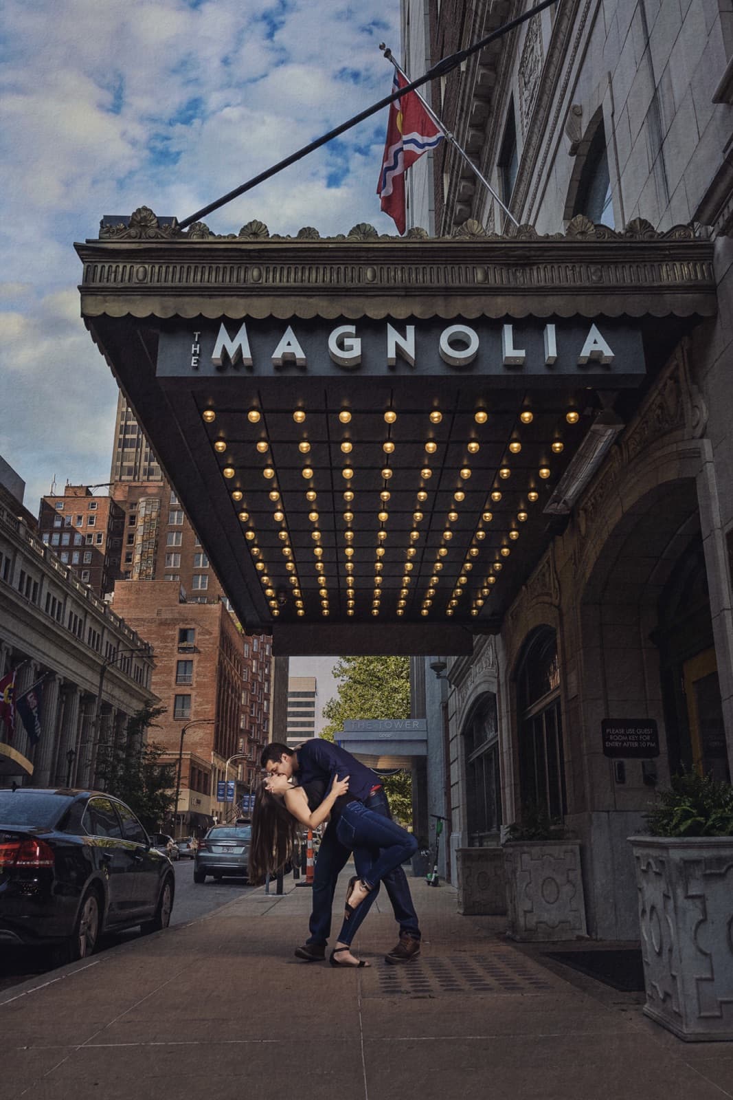 Couple sharing a playful dip kiss beneath the Magnolia Hotel marquee in downtown St. Louis