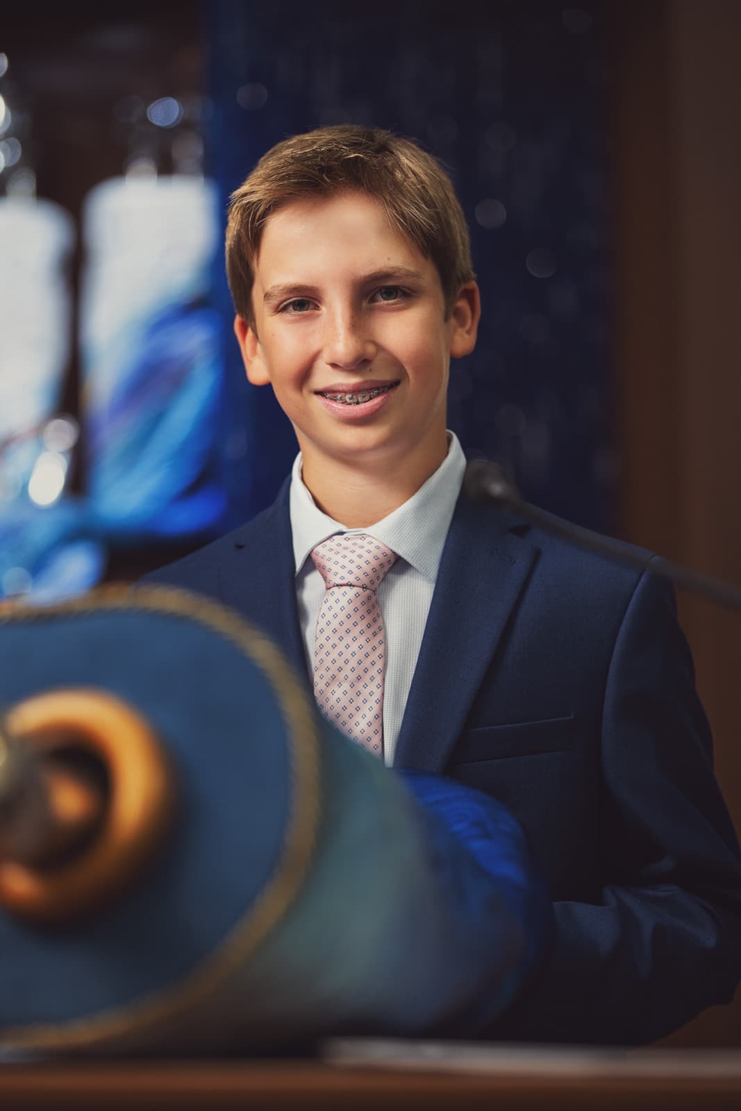 Bar mitzvah boy in a navy suit beside the Torah scroll at a St. Louis synagogue