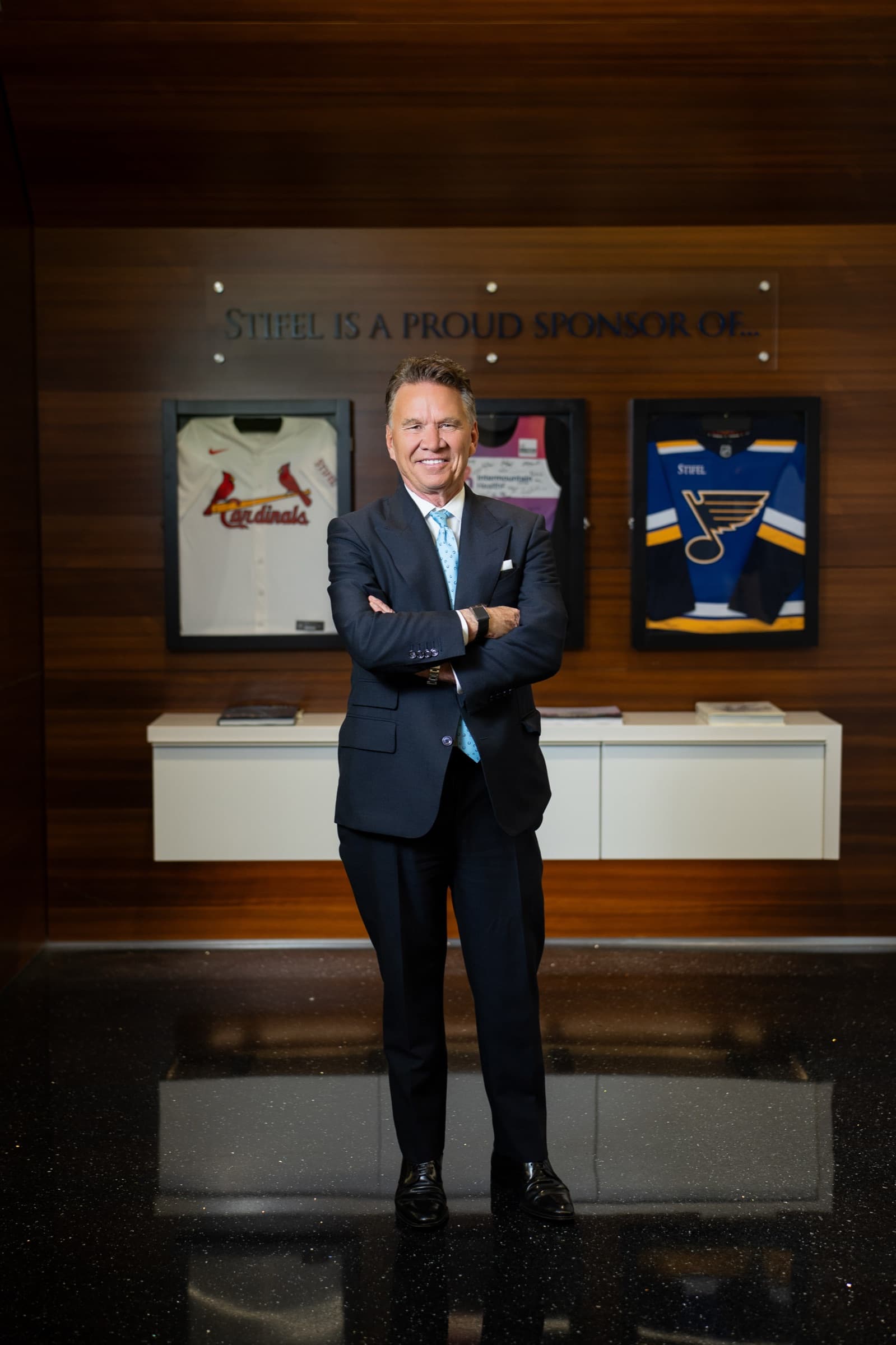 Executive in a dark suit and light blue tie standing with arms crossed in a wood-paneled Stifel office in St. Louis